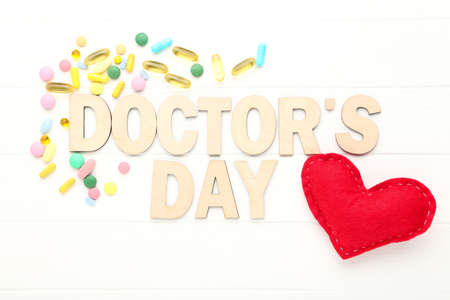 Text Doctor's Day with red fabric heart and colorful pills on white wooden tableの写真素材