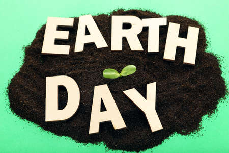 Soil with green sprout and text Earth Day on green background