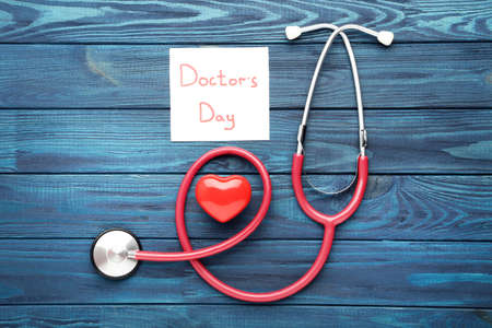 Stethoscope with red heart and text Doctor's Day on blue wooden tableの写真素材