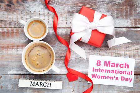 Two cups of coffee in shape of number 8 with text 8 March International Womens Day, gift and ribbon on wooden backgroundの写真素材