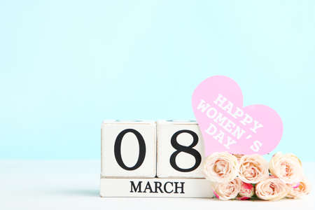 Rose flowers, card in shape of heart with text Happy Womens Day and wooden cube calendar on blue...