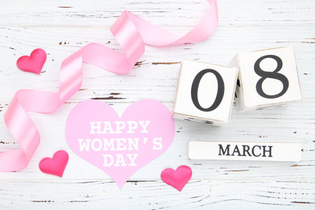 Cube calendar with pink card in shape of heart and text Happy Womens Day, hearts and ribbon on white...