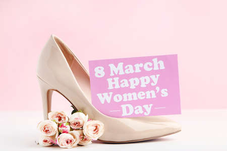 Rose flowers and card with text 8 March Happy Womens Day and high-heeled shoe on pink background