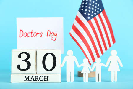 Text Doctor's Day with cube calendar, family figure and american flag on blue background