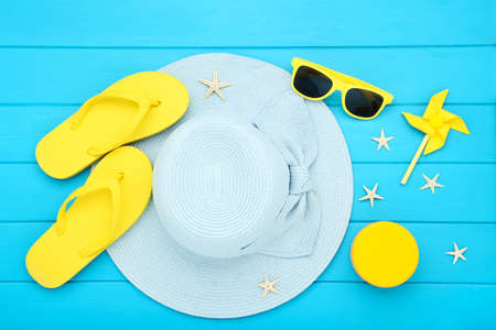 Summer straw hat with sunglasses, flip flops, windmill and starfishes on blue wooden tableの写真素材