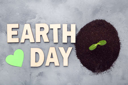 Soil with green sprout and text Earth Day on gray background