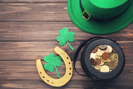 St. Patrick's hat with pot of coins, golden horseshoe and clover leafs on brown wooden background