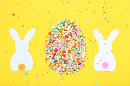Easter concept. Paper rabbits with colorful sprinkles on yellow background