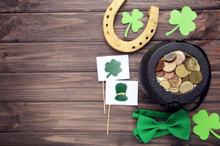 Pot of coins with golden horseshoe, clover leafs, bow tie and flags with pictures on brown wooden...