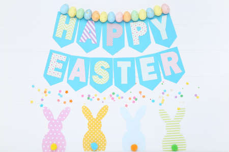 Text Happy Easter with colorful eggs and paper rabbits on wooden table