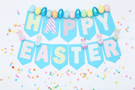 Text Happy Easter with colorful eggs and sprinkles on wooden table