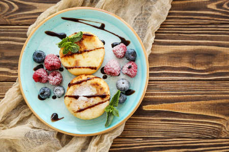 Sweet cheese pancakes with berries and mint leafs on wooden tableの写真素材