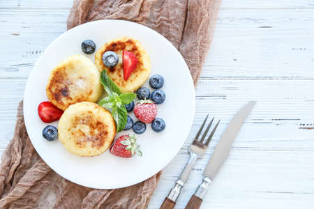 Sweet cheese pancakes with berries and cutlery on wooden tableの写真素材