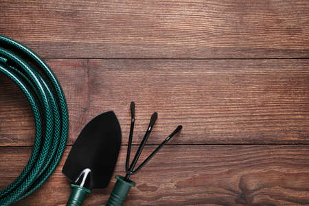 Garden shovel, rake and green hose on wooden table