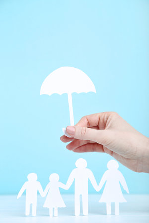 Family figures and female hand holding paper umbrella on blue backgroundの写真素材