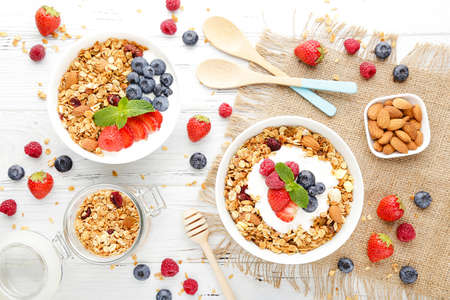Tasty granola with fresh berries and spoons on white wooden backgroundの写真素材