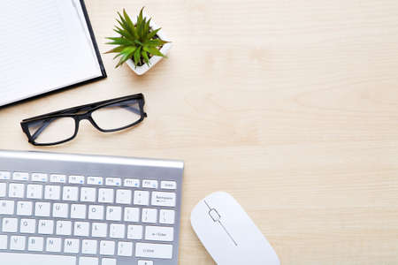 Computer keyboard with mouse, glasses and notepad on wooden table