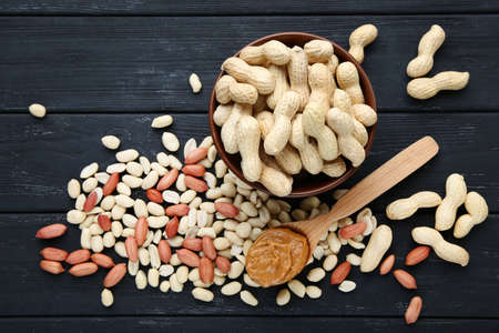 Peanut butter in spoon and nuts on black wooden table