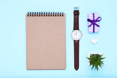 Father's day concept. Notepad with wrist watch, gift box and green plant on blue backgroundの写真素材