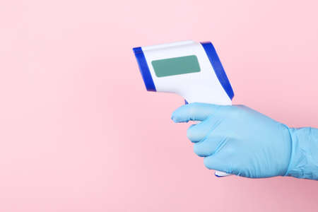 Infrared thermometer in doctor hand on pink background