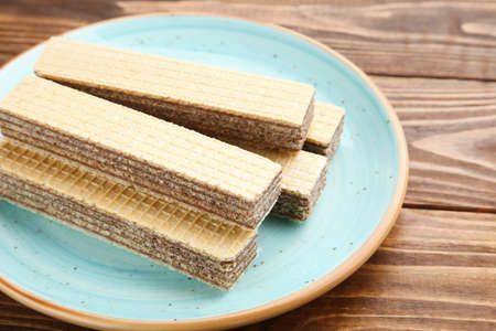 Sweet wafer sticks in plate on brown wooden background