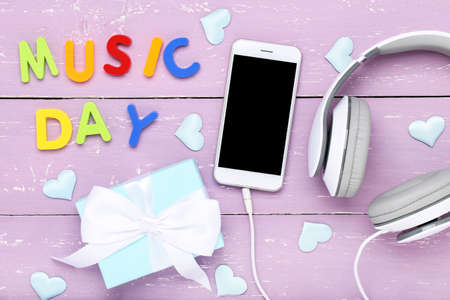 Headphones with smartphone, gift box and colorful text Music Day on purple wooden background