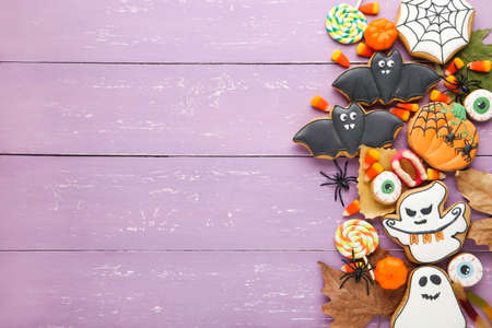 Halloween gingerbread cookies with candies, spiders and dry leafs on purple wooden tableの写真素材