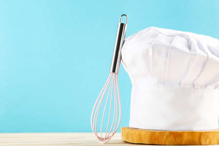 Chef hat on wooden cutting board with pink whisk on blue backgroundの写真素材