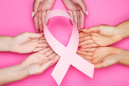 Breast cancer concept. Group of people in hands holding pink paper ribbon