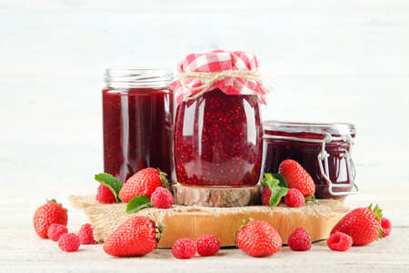 Sweet jam in glass jars with ripe berries on white background