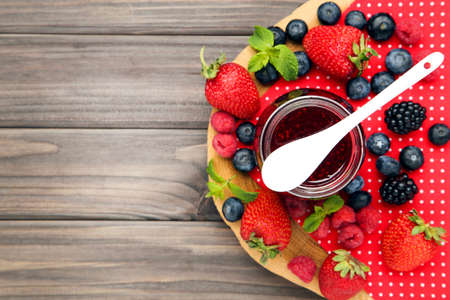 Sweet jam in glass jar with spoon and fresh berries on wooden table