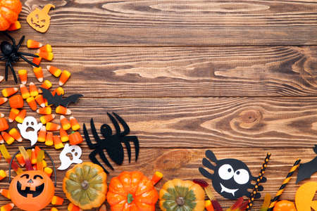 Halloween pumpkins, candies, spiders, ghosts and straws on brown wooden tableの写真素材