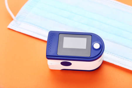 Pulse oximeter with medicine mask on orange background