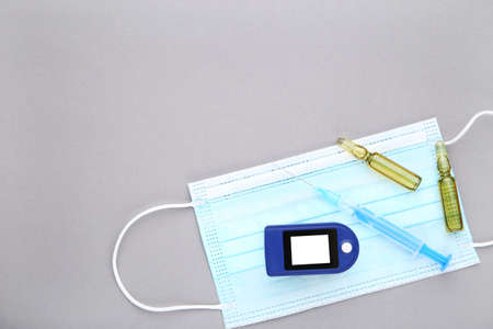 Pulse oximeter with syringe, ampoules and medicine mask on grey background
