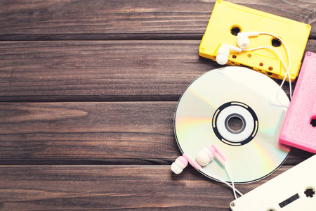 Cassette tapes with earphones and cd disk on wooden background