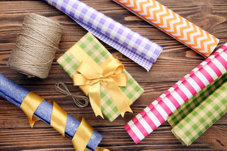 Rolls of craft papers with rope and gift box on brown wooden background
