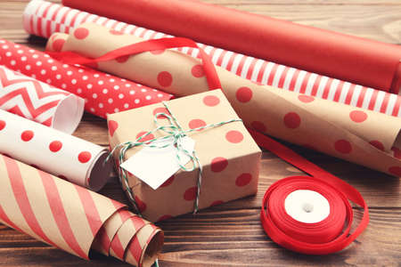 Rolls of craft papers with gift box and red ribbon on brown wooden background