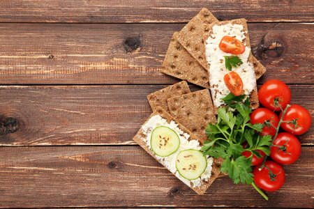 Crispbread with cream cheese, vegetables and green parsley on brown wooden tableの写真素材