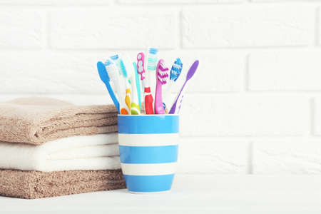 Colorful toothbrushes in cup and stack of towels on brick wall backgroundの写真素材
