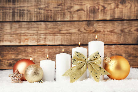 Christmas candles with ornaments and white snow on brown wooden backgroundの写真素材