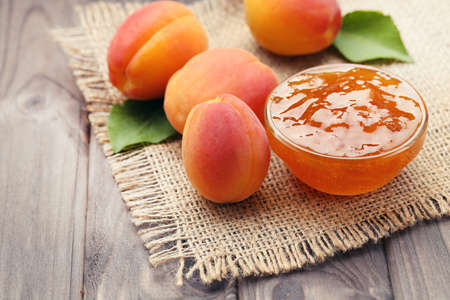Jam in bowl and apricots on brown wooden tableの写真素材