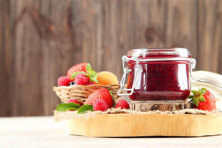 Sweet jam in glass jar with ripe berries on wooden background