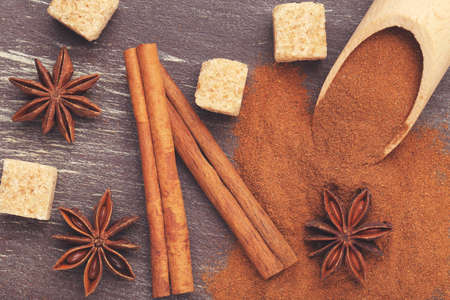 Cinnamon powder with sticks, star anises and sugar on brown wooden backgroundの写真素材