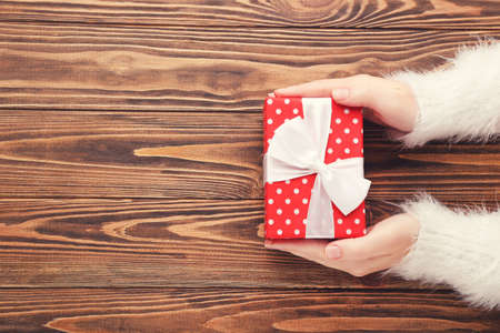 Female hands holding gift box on brown wooden backgroundの写真素材
