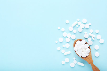 Medicine pills in wooden spoon on blue backgroundの写真素材