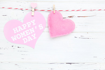 Pink card with text Happy Women's Day and felt heart hanging on rope on white wooden background