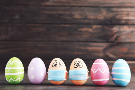 Row colorful easter eggs painted and in medical mask with funny faces on dark wooden backgroundの写真素材