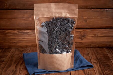 Organic dried fruits - dark raisins in craft eco packaging on a textural design background and linen textiles. Vegetarian food.の写真素材