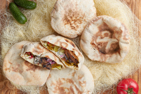 Kebab in pita with vegetables, top view, wooden background
