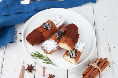Beautiful delicious french eclairs set with original cream decor on white plate on wooden...